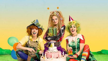 Drei Personen aus dem Ensemble "Der Traumzauberbaum - Das Geburtstagsfest" sitzen verkleidet auf dem Boden